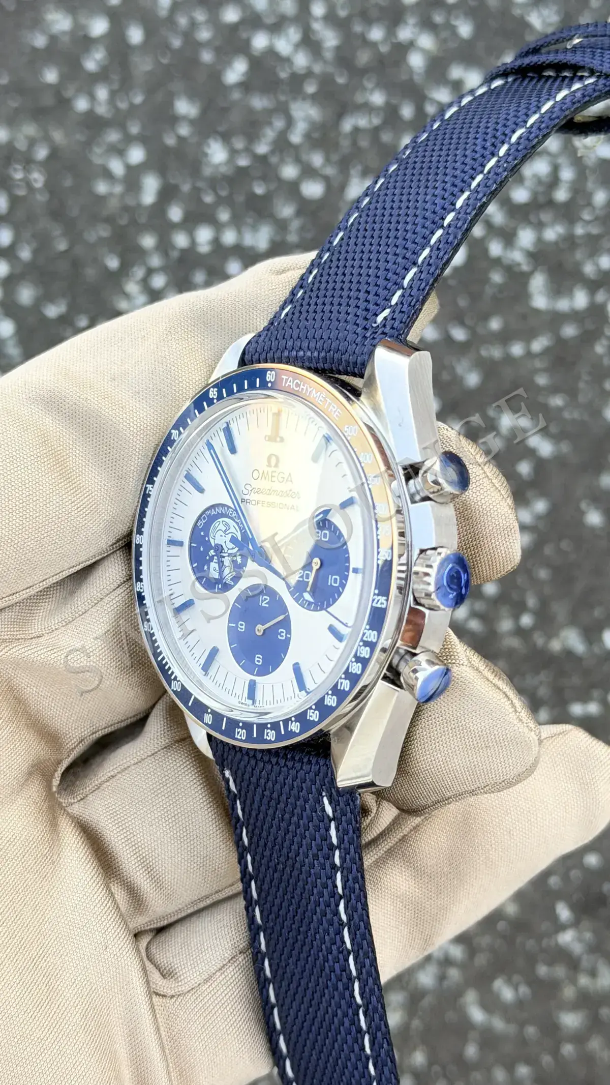 Omega Speedmaster Silver Snoopy Award Anniversary 50th No. 02, beyaz kadranda mavi alt sayaçlar ve takimetre ölçeği